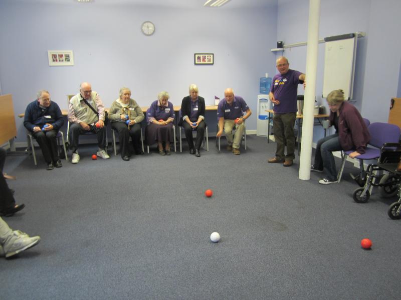 Large group of people sitting down in a room and playing a ball game