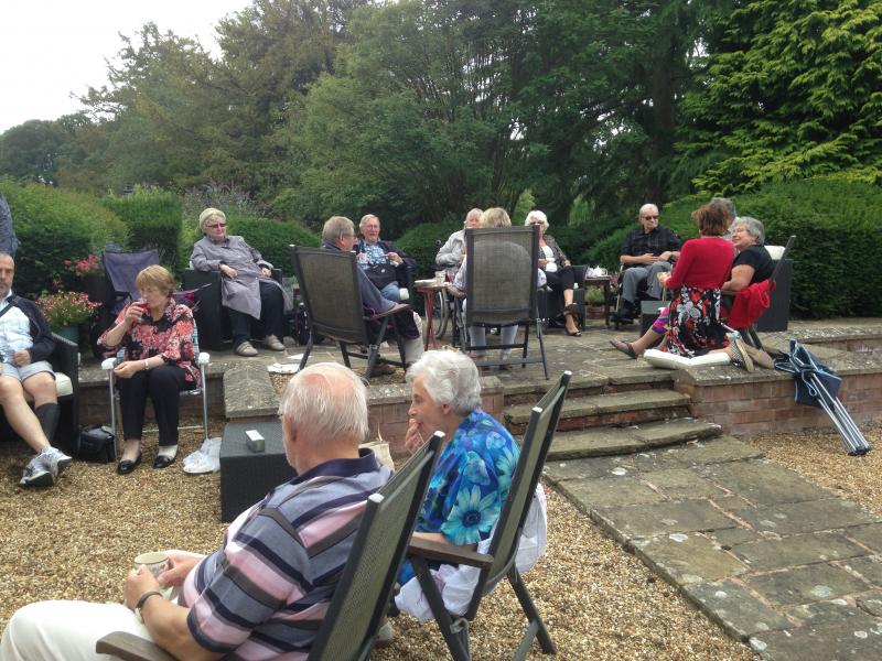 Large group of people sitting in chairs, in a garden