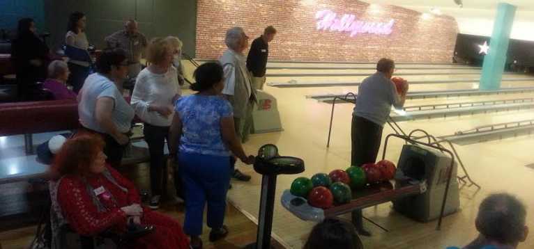 Several people at a bowling alley, some of them watching a man about to bowl.