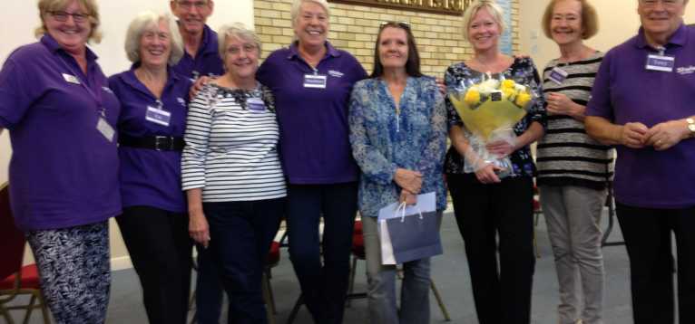 Several group members standing together. One woman is holding a bouquet of flowers.