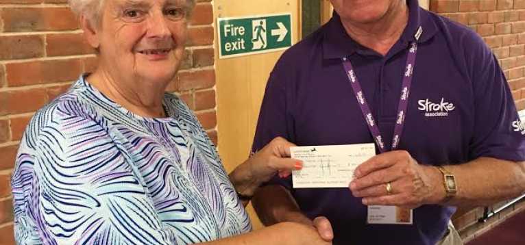 A woman handing a check to a man in a Stroke Association purple top, whilst they shake hands.