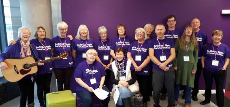 Large group of people standing, most wearing purple shirts which say: Northwest Community Stroke Choir.