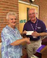 A woman handing a check to a man in a Stroke Association purple top, whilst they shake hands.
