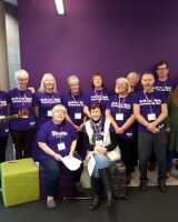 Large group of people standing, most wearing purple shirts which say: Northwest Community Stroke Choir.