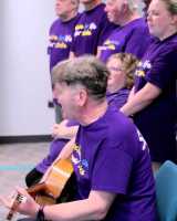 A group singing with a guitarist in purple stroke association t-shirts
