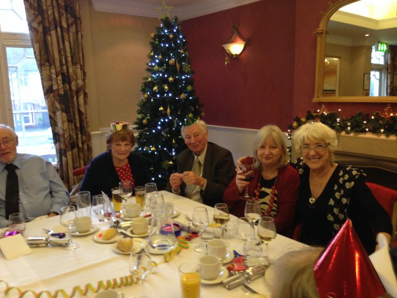 Five people sitting at a table with decorations on it, with a Christmas tree behind them